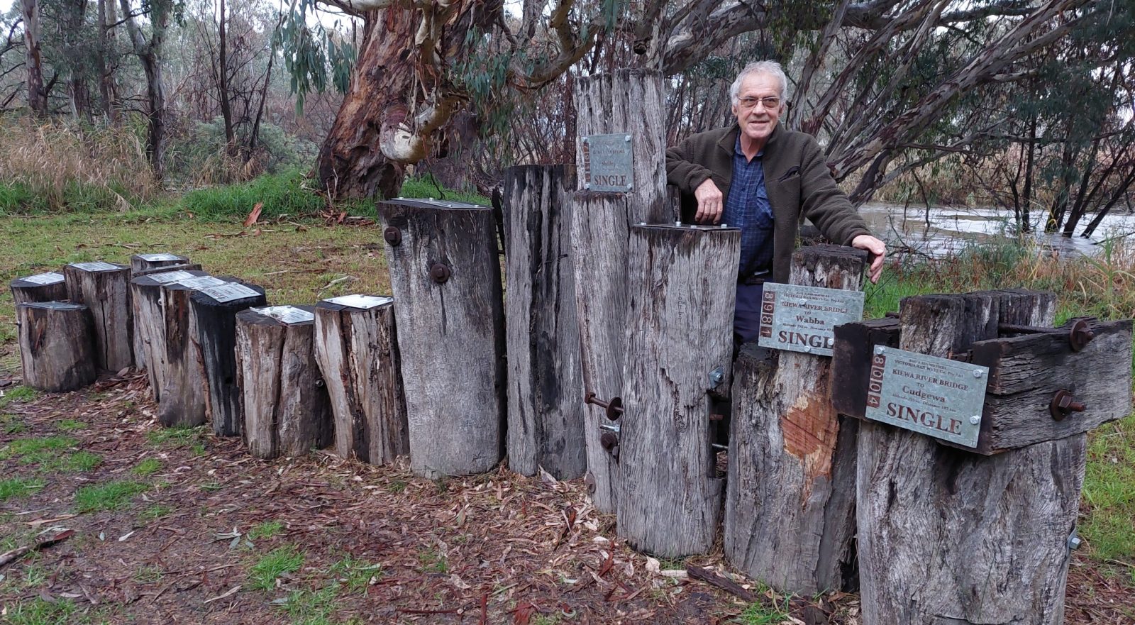 The artist Max Laubli standing behind his sculpture. The sculpture is made of upright old timber bridge posts, placed at duifferent heights to represent the different heights of the railway stations on the line.
